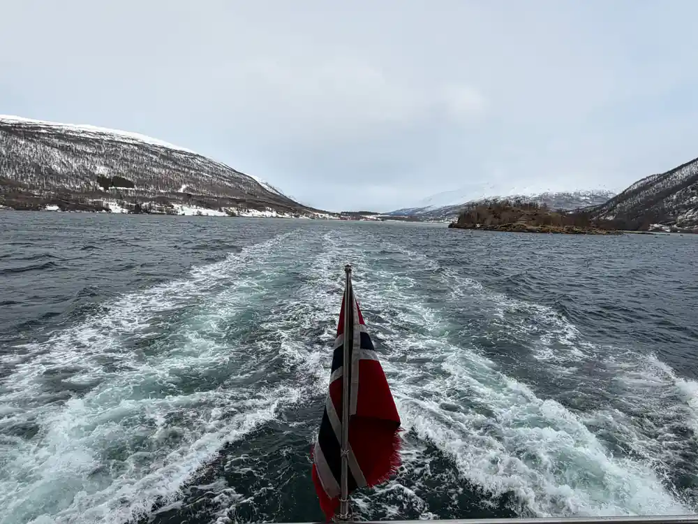 Boat wake in fjord with snow-covered mountains on either side