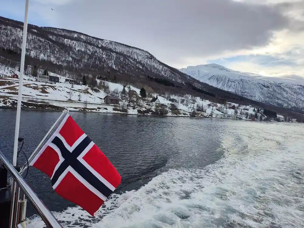 Norwegian flag on ship with snowy fjord landscape