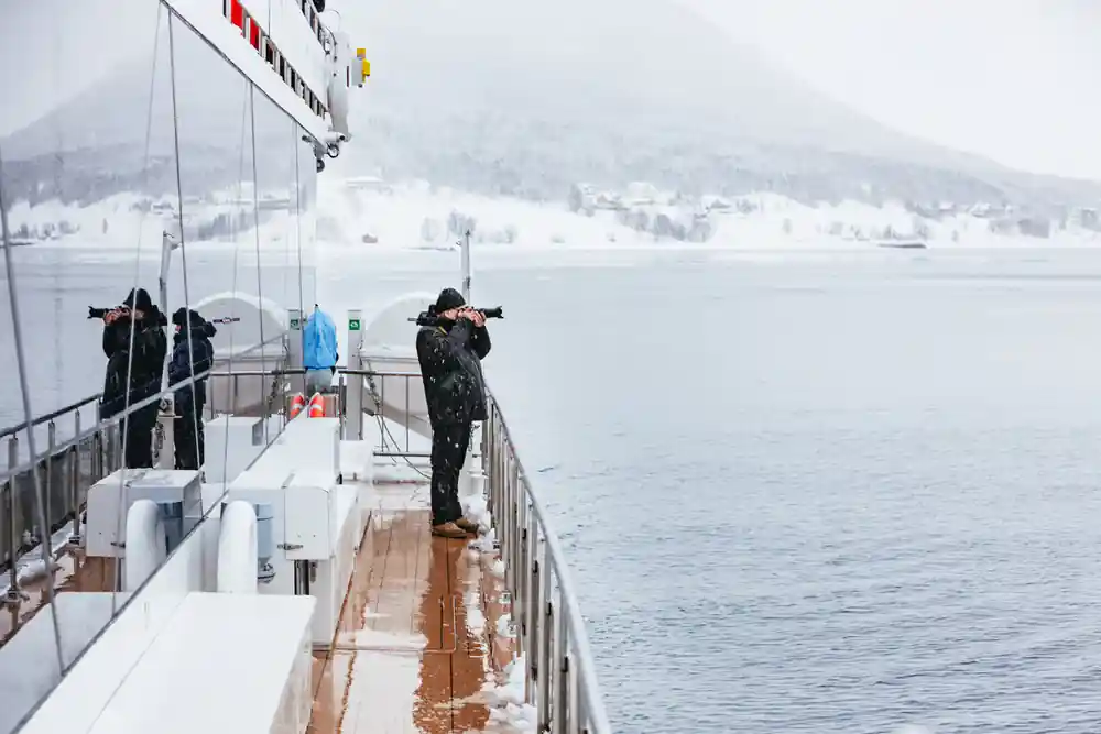 People on ship deck photographing snowy mountainous landscape