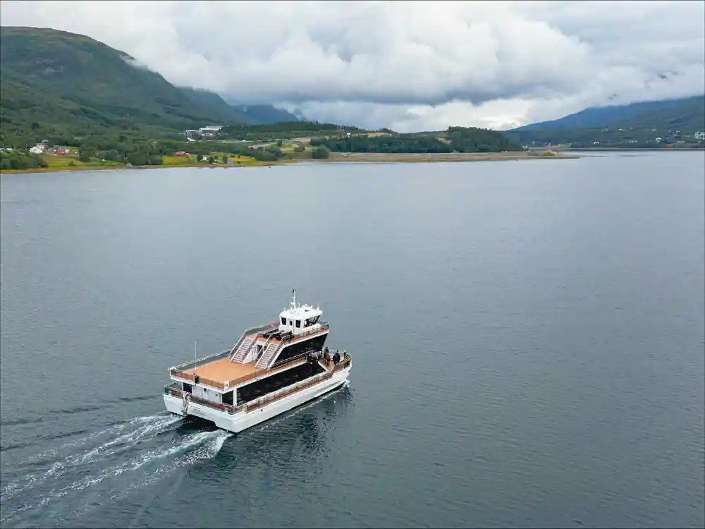 Small motorboat moving on calm water between green mountains