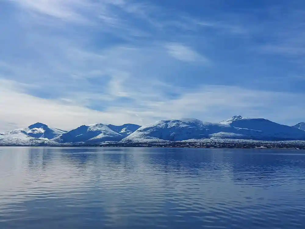 Snow-capped mountain range across calm blue fjord water