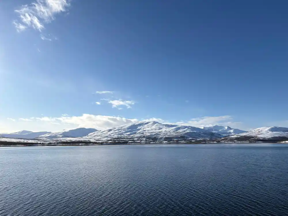 Snow-capped mountains reflected in still fjord water at distance