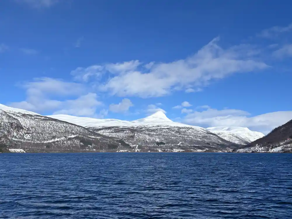 Snow-covered mountains across blue water in sunlight