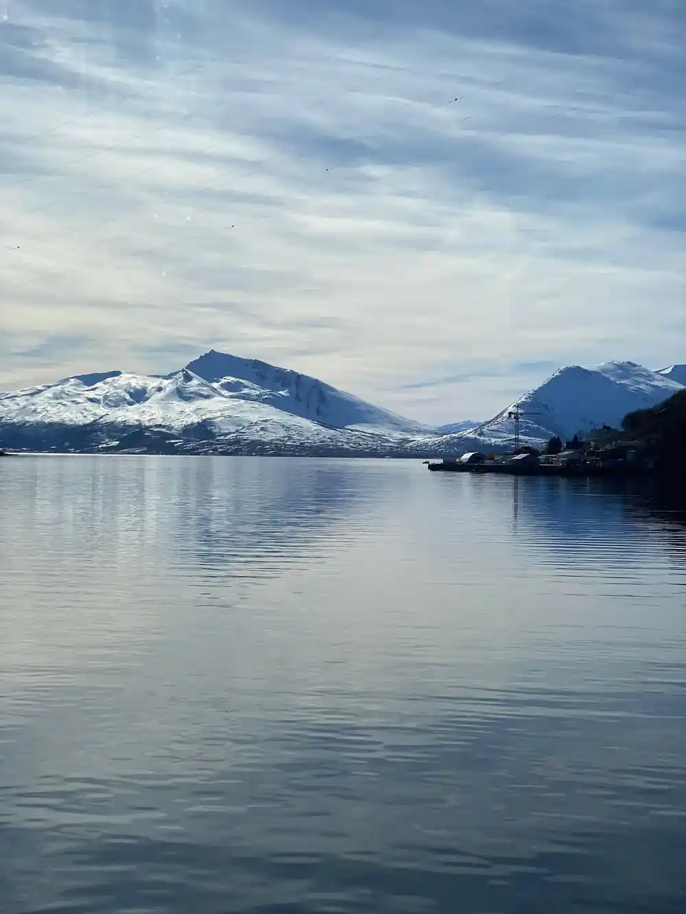Snow-covered mountains reflected in still fjord water