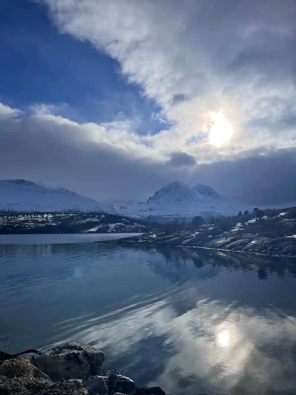 Snow-covered mountains reflected in still fjord water