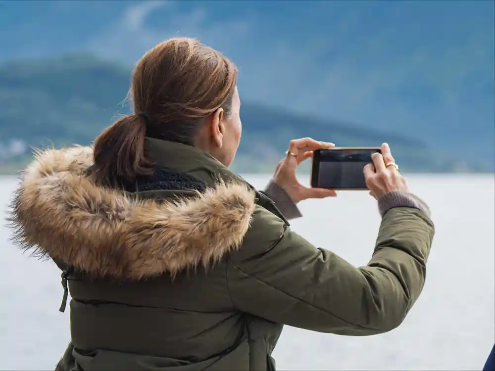 Woman in winter coat taking photo with smartphone